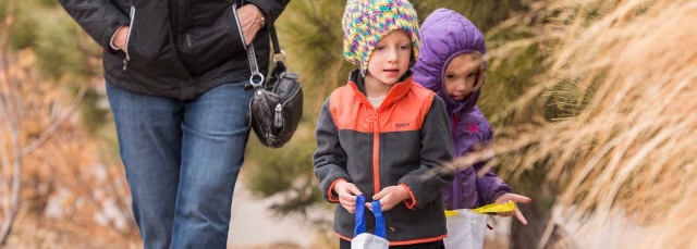 Two children looking at grasses with an adult behind them. 